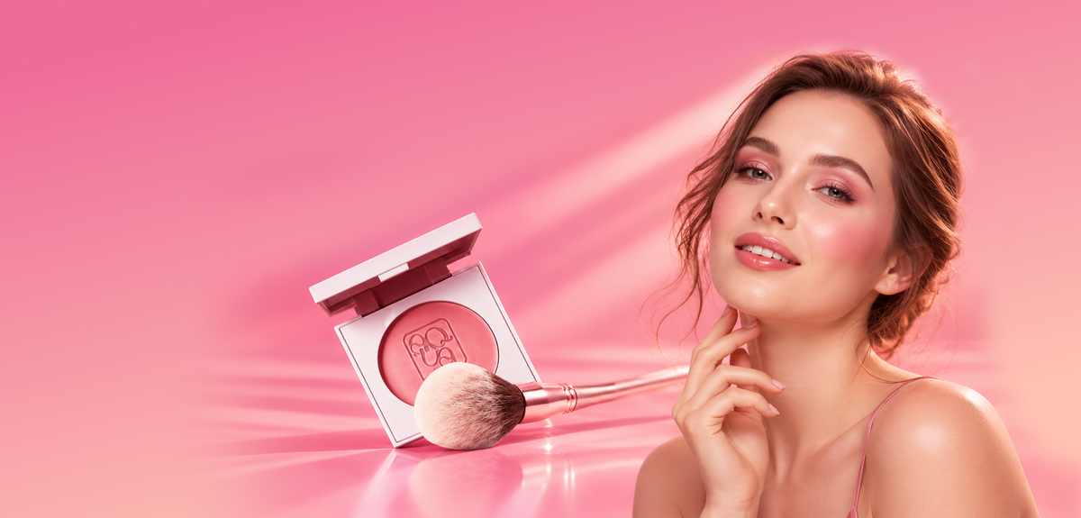 A woman with pink-toned makeup and a blush compact beside an open powder blush compact with a brush, set against a bright pink studio background.